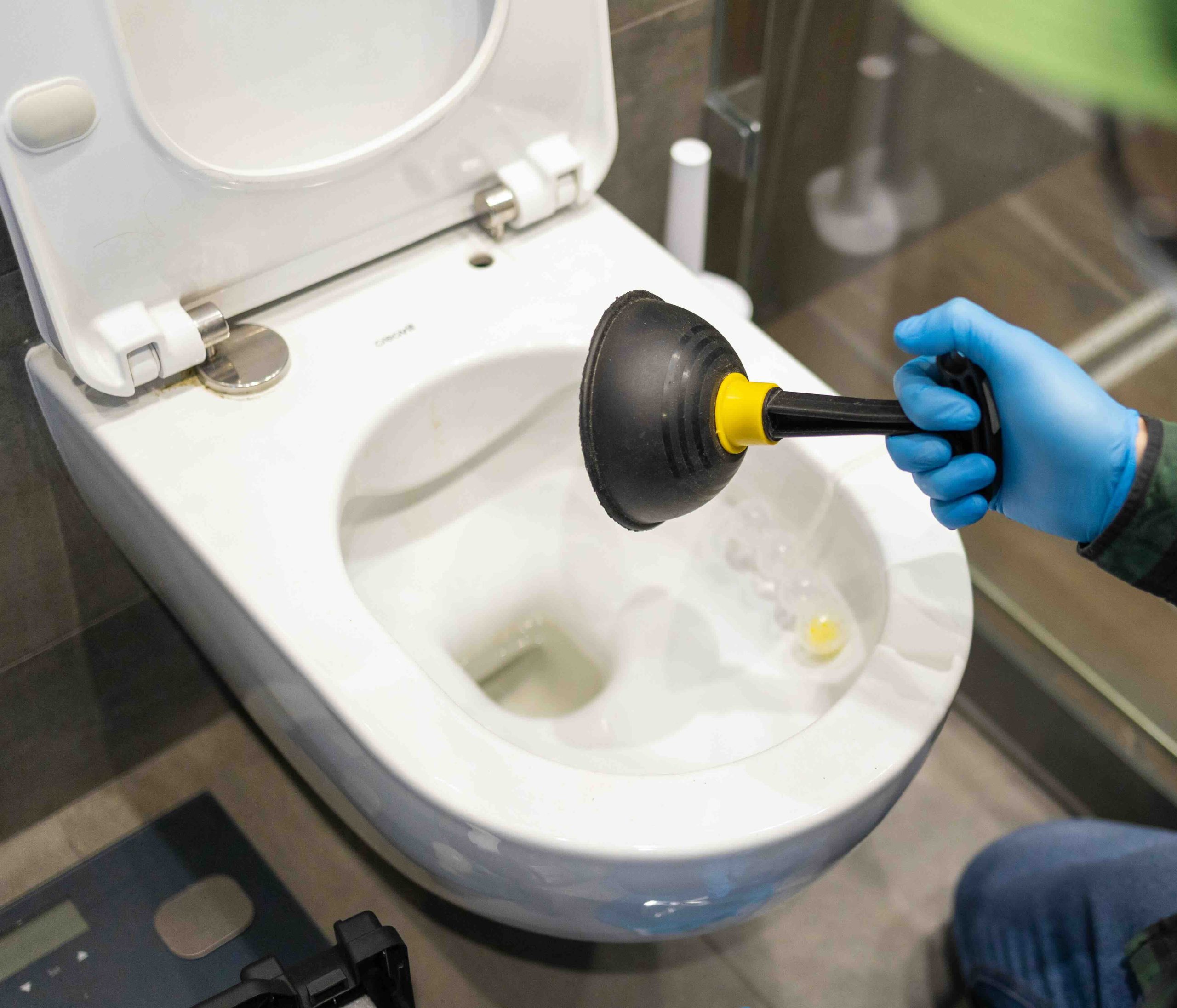 A repair man unclogging a toilet with a plunger.